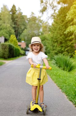 Mutlu küçük kız sarı etek beyaz gömlek tekme açık, öğrenen dengesi, yaz saati, güneş ışığı, pembe kask giyiyor sürme