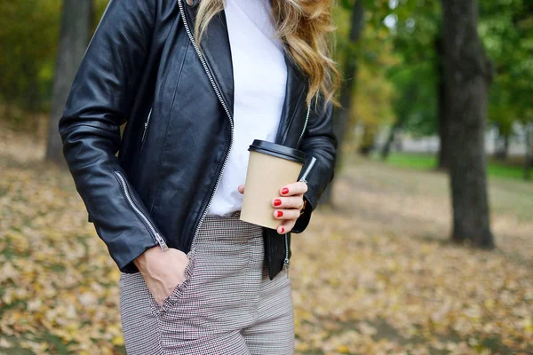 秋の公園で歩いているかなり若い女性リラックス レジャー黒革ジャケット ファッション現代赤い爪飲みコーヒーを離れて — ストック写真