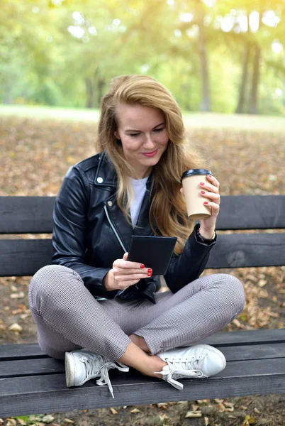 Genç ve güzel kadın sonbahar Park'ta yürüyordunuz rahatla kahve almak uzakta Kupası içme eğlence siyah deri ceket moda Modern kırmızı çivi