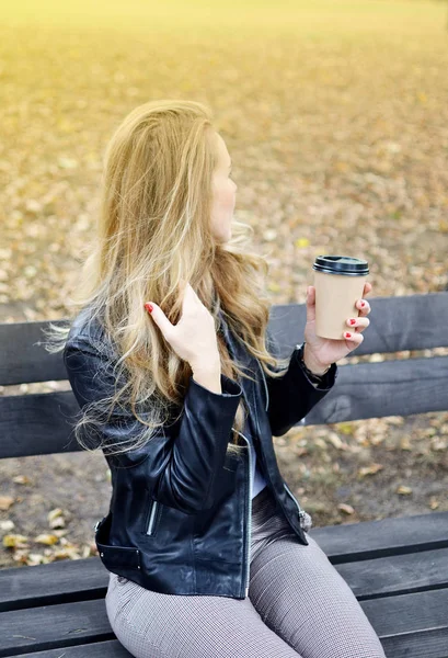 Genç ve güzel kadın sonbahar Park'ta yürüyordunuz rahatla kahve almak uzakta Kupası içme eğlence siyah deri ceket moda Modern kırmızı çivi