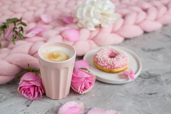 Cup with cappuccino, doughnut, pink pastel giant blanket, flowers, bedroom, morning concept