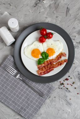 Lezzetli kızarmış yumurta bir kalp şeklinde hizmet pastırma domates fesleğen karabiber gri arka plan Valentine ile beyaz bir plaka üzerinde gün kahvaltı
