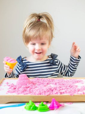 Eve erken eğitim okul geliştirme çocuk oyunu için hazırlanıyor pembe Kinetik kumla oynayan küçük mutlu beyaz kız