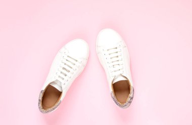 Pastel pembe arka planda beyaz spor ayakkabıları. Düz yatıyordu, üstteki görünüm minimal arka plan
