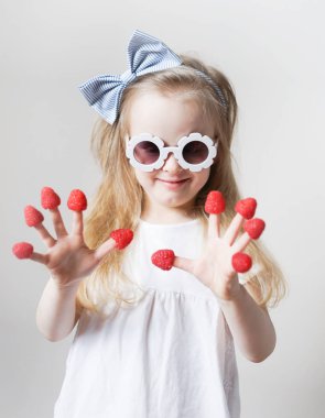 Parmaklarında ahududu ile küçük sevimli sarışın kız, farklı duygular, kapalı, sağlıklı gıda yaz kavramı