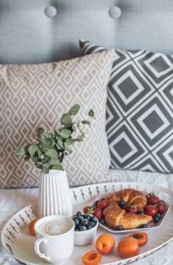 Yatakta sabah kahvaltısı, bir fincan kahve, kruvasan, taze çilek, sulu tencere. Sağlıklı gıda kavramı. İskandinav tarzı