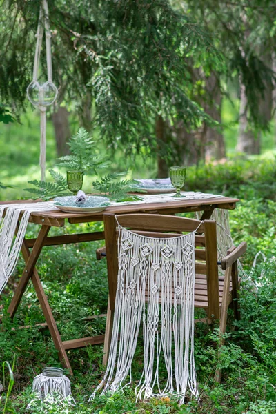 Boho style wedding reception dinning table with macrame tablecloth, decoration on a rustic wooden table