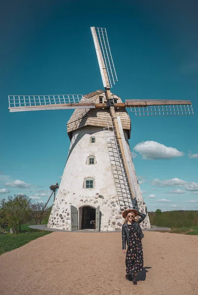 Woman in hat looking at old wildmill building, summer sunny day, Latvia, Vidzeme