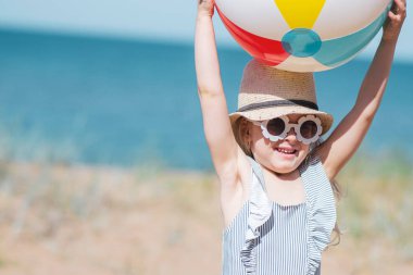 Şapkalı küçük kız plajda top ile oynuyor, güneşli yaz günü. Tatil konsepti
