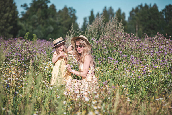 Cute little girl with her mother walking in the flowers field with, family look, summer time, mother's day