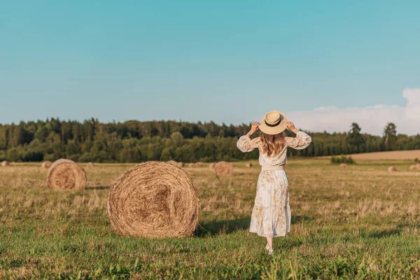 Woman walking in field with haystacks, summer time, countryside