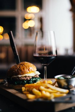 Kızarmış yumurta ıspanak ve et pirinci ile lezzetli lezzetli kokulu altın susam burger hazırlayın kırmızı şarap bir bardak yanında bir masaya yerleştirilir ve bir bıçak odak sıkışmış altın patates kızartması, orta mesafe 