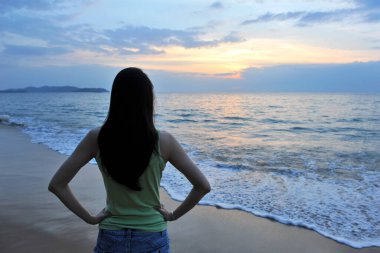 Sahilde Günbatımında Gökyüzünü ve Denizi seyreden Bir Kadının Silueti