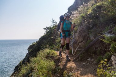 Kız turist Baykal Gölü üzerinde kayalık bir iz üzerinde gidiyor