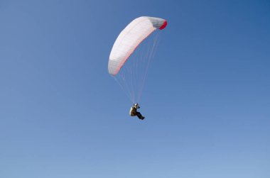 Adam bir paraşüt ile atlama, mavi gökyüzü arka planda bir yamaç paraşütü yapıyor