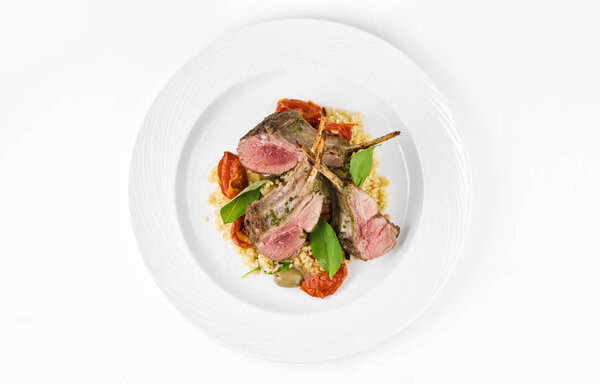Rack of lamb with bulgur, dried tomatoes and lemon Moroccan on a plate on a white background, top view