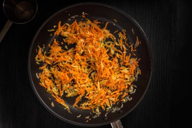 Koyu arka planda tavada kızarmış soğan ve havuç, üst görünüm