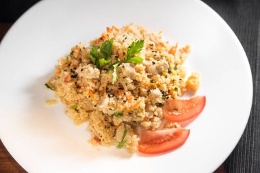 Koyu arka planda beyaz bir plaka üzerinde ızgara tavuk, soğan, havuç ve domates ile kuskus