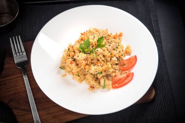 Koyu arka planda beyaz bir plakada ızgara tavuk, soğan, havuç ve domates ile kuskus, üst görünüm