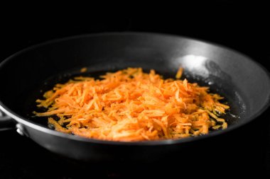 Kuru havuç siyah bir arka planda bir kızartma tavasında bitkisel yağda kızartılır, çekim