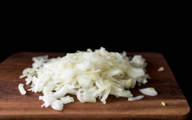 Siyah bir arka planda ahşap bir tahta üzerinde ince doğranmış soğan, çekim