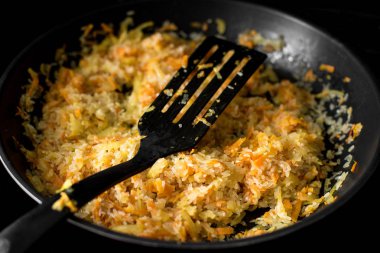 Siyah bir arka planda bir kızartma tavasında bitkisel yağda doğranmış soğan, havuç ve pirinç kızartması, çekim