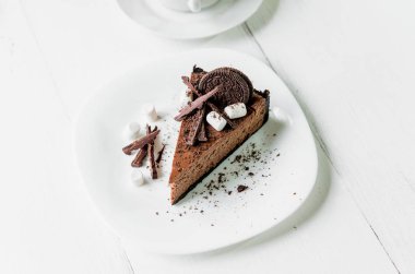 Çikolatalı cheesecake ile çikolata, kurabiye ve Marshmallow masada bir fincan çay yanında beyaz bir plaka üzerinde
