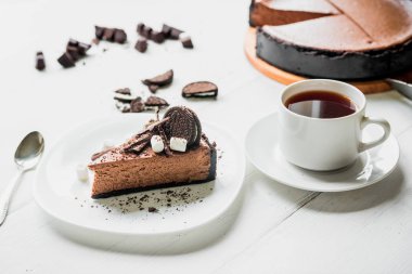 Çikolatalı cheesecake ile çikolata, kurabiye ve Marshmallow masada bir fincan çay yanında beyaz bir plaka üzerinde