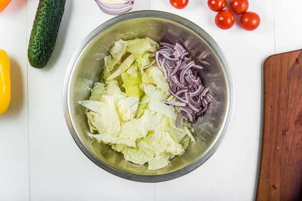 Salad preparation: iceberg salad, Peking cabbage and chopped red onion in a metal bowl, top view