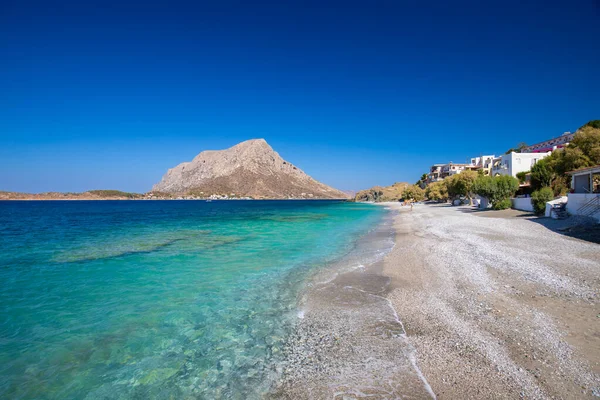 Yunanistan 'ın Telendos adasında, açık mavi gökyüzünün altında turkuaz su ve dağlarla kaplı bir sahil.