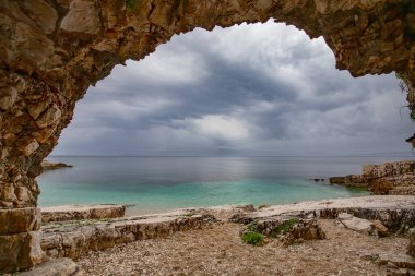 Gök mavisi suları ve Kassiopi 'de resim gibi bir plajı olan körfez bulutlu bir günde, Yunanistan' ın Korfu adasında.