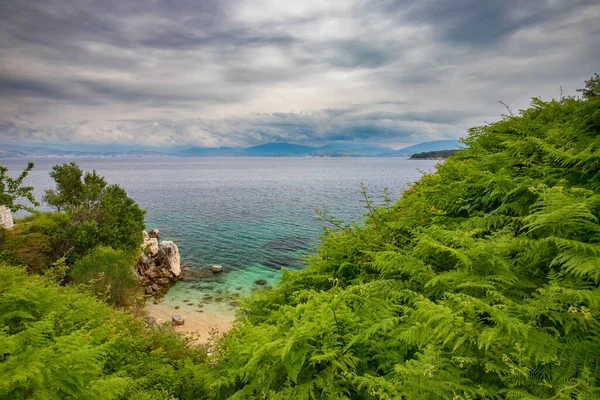 Gök mavisi suları ve Kassiopi 'de resim gibi bir plajı olan körfez bulutlu bir günde, Yunanistan' ın Korfu adasında.