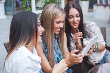 Grup Genç neşeli kadınların tablet vasıl seyir ve açık havada online alışveriş yapma