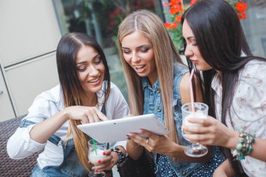 Grup Genç neşeli kadınların tablet vasıl seyir ve açık havada online alışveriş yapma