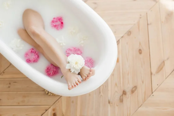 Women`s feet resting in the bath among beautiful flowers
