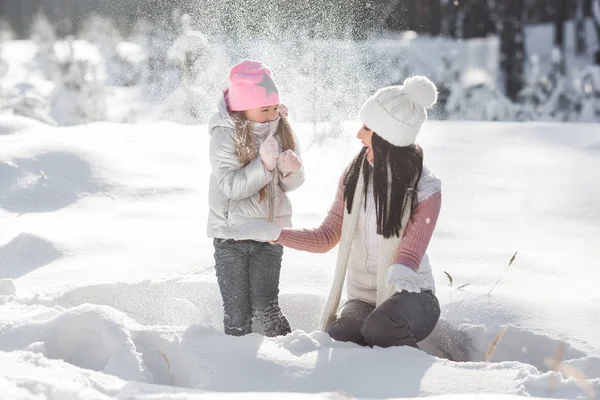 Genç güzel anne ve küçük kızı kışın dışarıda eğleniyor. Çocuk ve kar, doğa ile oynarken annesi güzel.