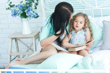 Kitap okumak için küçük şirin kızı öğretim güzel genç anne. Anne küçük çocuğunu iyi geceler masal okuma