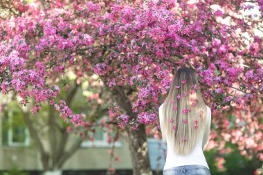 Saçında çiçekler ile uzun sarı saçlı kamera için arka yüzüne duran tanınmaz halde kadın. Erkek bahar arka plan üzerinde. Bayan açık havada.