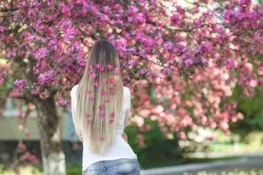 Saçında çiçekler ile uzun sarı saçlı kamera için arka yüzüne duran tanınmaz halde kadın. Erkek bahar arka plan üzerinde. Bayan açık havada.