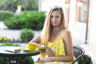 Çekici kadın kafeteryada. Sarı elbise giyen genç bayan. Neşeli kız açık havada içki kahve