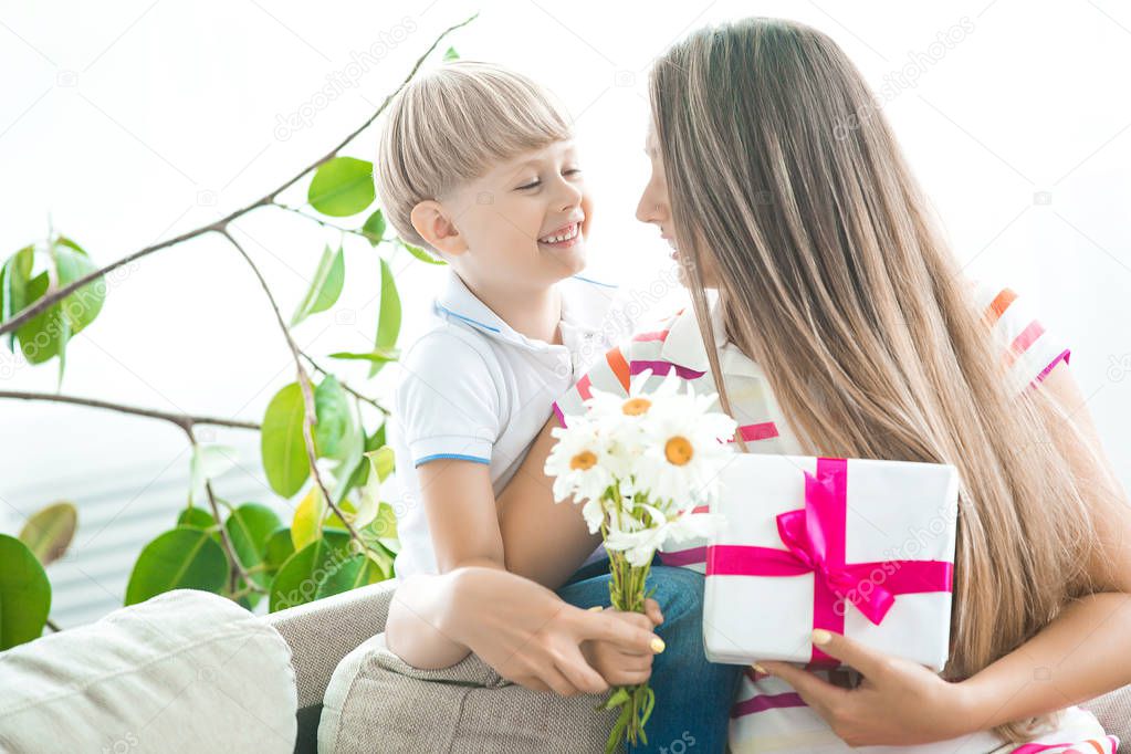 Cute little child congratulates his mother with mothers day. Adorable boy with is mom holding a present for 8th of march or birthday. Happy family celebrating