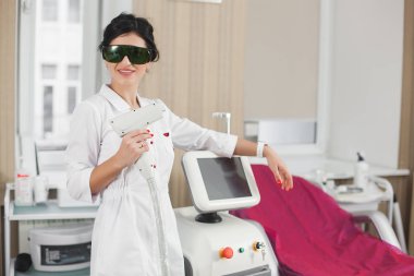 Kopya alanı olan lazer epilatörü olan çekici bir kozmetikçi. Güzellik salonunda tıbbi malzemelerle neşeli bir doktor. Klinikteki kozmetolog dermatolog..