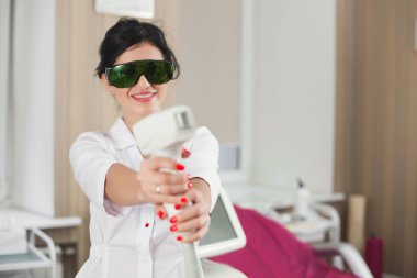 Lazer epilatör ekipmanlı çekici bayan kozmetikçi. Doktor dermatolog elinde bir epilatör tutuyor. Güzellik salonu veya klinikte profesyonel kozmetoloji prosedürü