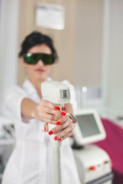 Lazer epilatör ekipmanlı çekici bayan kozmetikçi. Doktor dermatolog elinde bir epilatör tutuyor. Güzellik salonu veya klinikte profesyonel kozmetoloji prosedürü