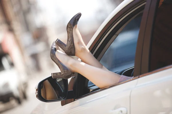 Woman`s feet in the car. Unrecognizable woman in the automobile. Lady`s shoes out of the car`s window. Female legs.