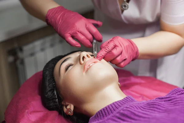 Procedure of lip augmentation in the beauty salon. Cosmetologist making an injection of hyaluronic acid to boost the lips. Woman in the cosmetological parlor