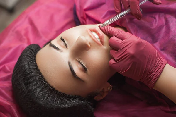 Procedure of lip augmentation in the beauty salon. Cosmetologist making an injection of hyaluronic acid to boost the lips. Woman in the cosmetological parlor