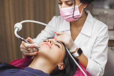 Çekici genç doktor müvekkiline mezoterapi yapıyor. Güzellik salonundaki kadın. Doktor tıbbi cihazlarla yüz tedavisi yapıyor. Klinikte elmas cilt soyma prosedürü.