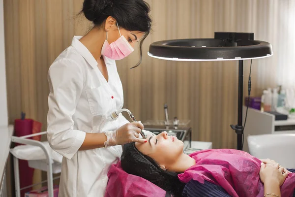 Attractive young doctor making mesotherapy to her client. Woman in the beauty salon. Doctor making face treatment with medical apparatus. Diamond skin peeling procedure in the clinic.