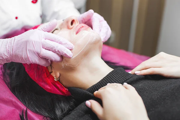 Cosmetologist making face care procedure. Specialist applying face mask to her client. Dermatology treatment. Facial peeling.